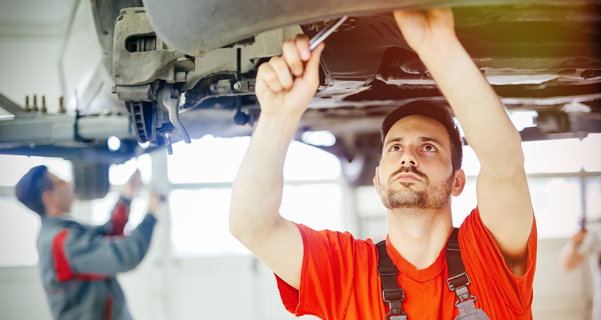 Mechanics working on MOT tests underneath cars on ramps in a garage